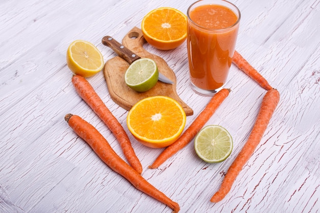 Orange detox coctail mit orangen, kalk und karotten liegt auf weißem tisch