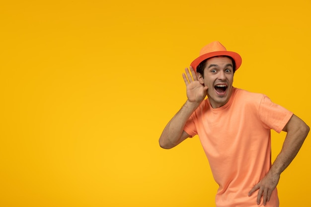 Orange Hut hübscher hübscher Kerl im orangefarbenen T-Shirt mit dem Hut, der aufregend lauscht