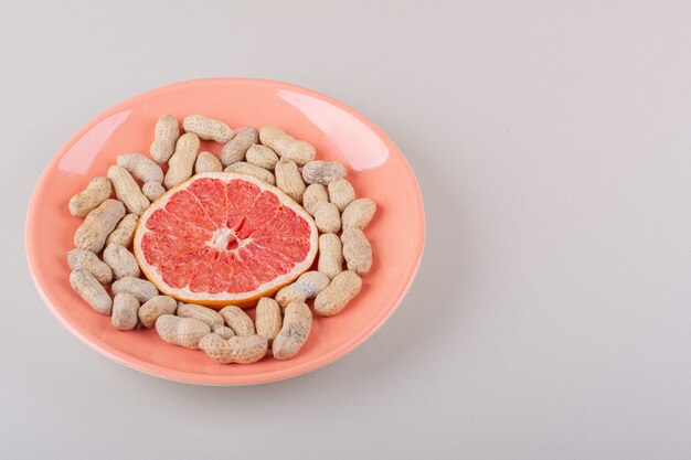 Orange Teller mit Grapefruitscheibe und Bio-Erdnüssen auf weißem Hintergrund. Foto in hoher Qualität