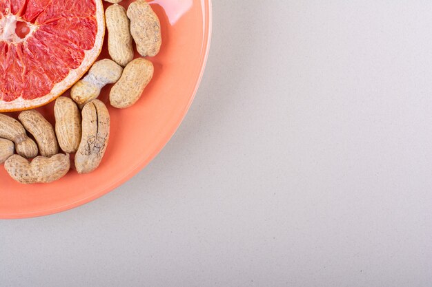 Orange Teller mit Grapefruitscheibe und Bio-Erdnüssen auf weißem Hintergrund. Foto in hoher Qualität