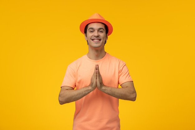 Orangefarbener Hut süßer junger Kerl im orangefarbenen Hemd mit betendem und lächelndem Hut