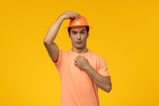 Orangefarbener hut, süßer junger kerl in orangefarbenem t-shirt, der ein lustiges gesicht macht und einen hut hält