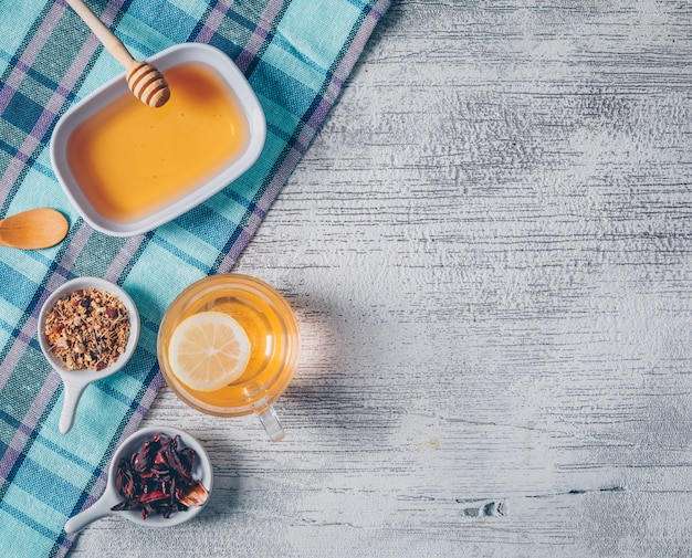 Orangefarbenes Wasser der Draufsicht mit Honig- und Teekräutern auf Picknicktuch und grauem hölzernem Hintergrund. horizontaler Raum für Text