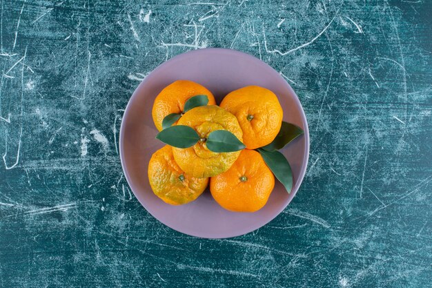 Orangen und Mandarinen auf einem Teller auf dem Marmortisch.