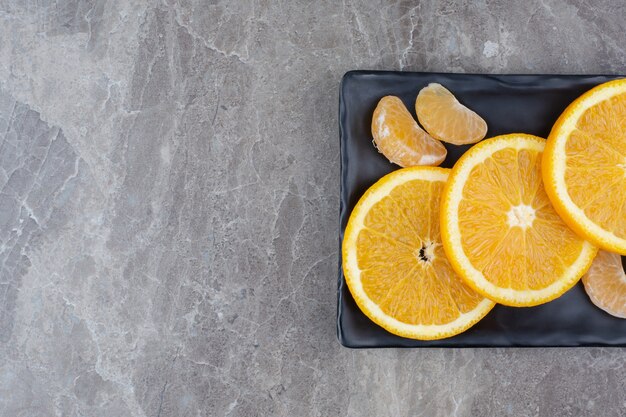 Orangen- und Mandarinenscheiben auf schwarzem Teller.