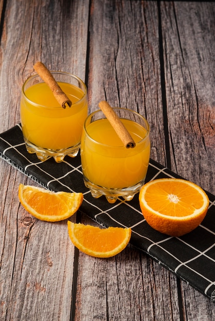 Kostenloses Foto orangenfrucht mit einem glas saft und zimtstangen auf schwarzem handtuch