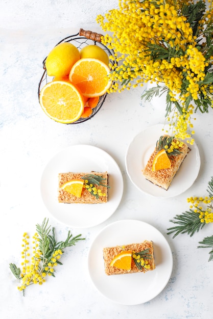 Orangenkuchen dekoriert mit frischen Orangenscheiben und Mimosenblüten auf Licht