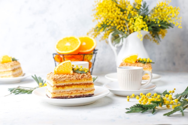 Orangenkuchen dekoriert mit frischen Orangenscheiben und Mimosenblüten auf Licht