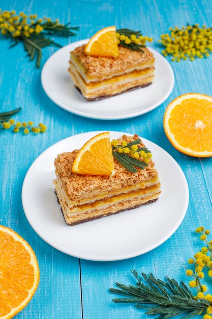 Orangenkuchen dekoriert mit frischen Orangenscheiben und Mimosenblüten auf Licht