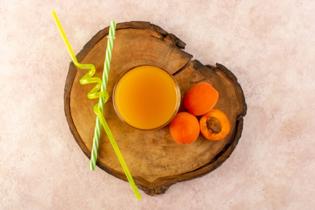 Orangensaft der Draufsicht in kleinem Glas mit Strohhalmen und frischer Abkühlung der frischen Orangen Aprikosen lokalisiert auf dem braunen hölzernen Schreibtisch und rosa Hintergrundtrinkfrucht