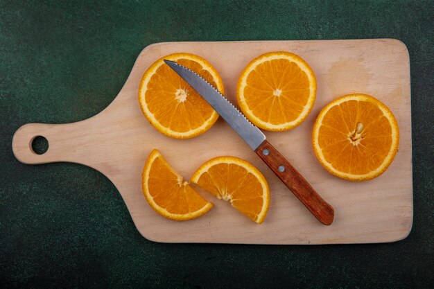 Orangenscheiben der Draufsicht auf Schneidebrett mit Messer auf grünem Hintergrund