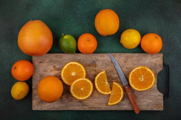 Orangenscheiben der Draufsicht auf Schneidebrett mit Messer Zitronenlimette und Grapefruit auf grünem Hintergrund