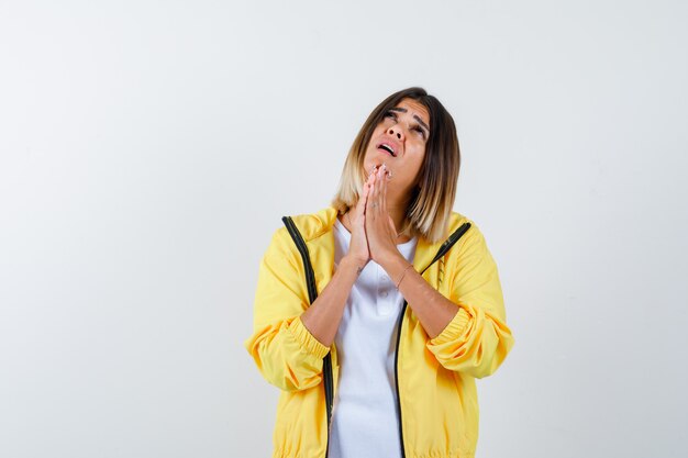 Ortrait der Frau, die Hände in der Gebetsgeste im T-Shirt, in der Jacke und in der hoffnungsvollen Vorderansicht hält