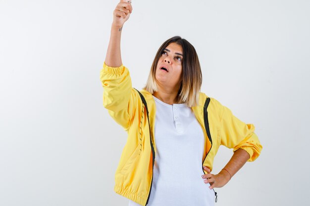 Ortrait der Frau, die im T-Shirt, in der Jacke und in der fokussierten Vorderansicht nach oben zeigt