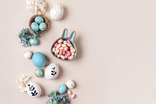 Ostereier mit süßigkeiten und blumen auf beige fröhliches osterkonzept weiße und blaue eier mit süßem teller in form eines häschens Premium Fotos