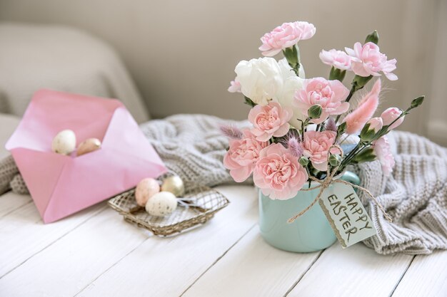 Osterkomposition mit frischen Blumen in einer Vase, einem gestrickten Element und der Aufschrift Frohe Ostern auf der Karte.