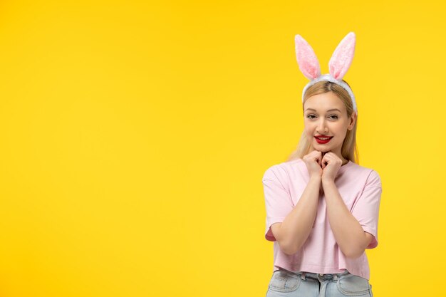 Ostern entzückendes hübsches junges blondes Mädchen mit Hasenohren, das glücklich die Hände unter dem Kinn hält