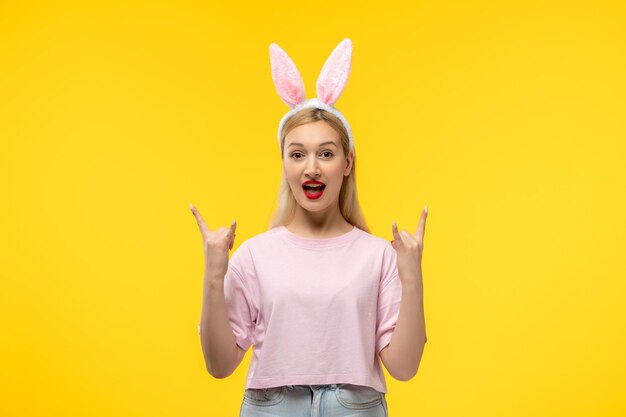 Ostern schönes süßes blondes Mädchen mit Häschenohren, das lächelt und Rockzeichen zeigt