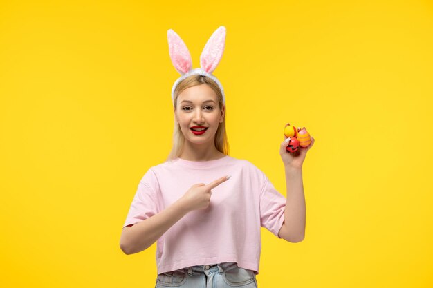 Ostern süßes junges blondes Mädchen mit rosafarbenen Hasenohren, das glücklich lächelt und Ostereier hält