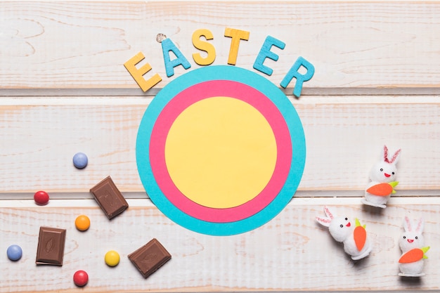 Ostern-Wort auf rundem Papierrahmen mit Häschen; Schokoladenstücke und Edelsteine auf hölzernen Hintergrund