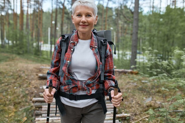 Outdoor-Aktivitäten, Menschen und Urlaubskonzept. Attraktive kurzhaarige Frau mittleren Alters in Aktivkleidung, die im Wald mit Stöcken für Nordic Walking wandert, Aerobic-Training macht, Natur genießt