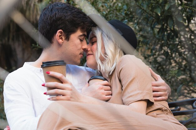 Paar beugt sich für einen Kuss vor, während es draußen auf einer Bank bleibt