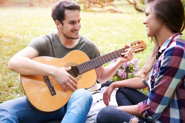 Paar genießt ein Picknick im Park. Mann spielt Gitarre. Romantisches Date