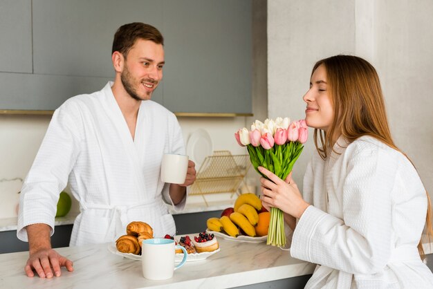 Paar im Bademantel in der Küche mit Strauß Tulpen