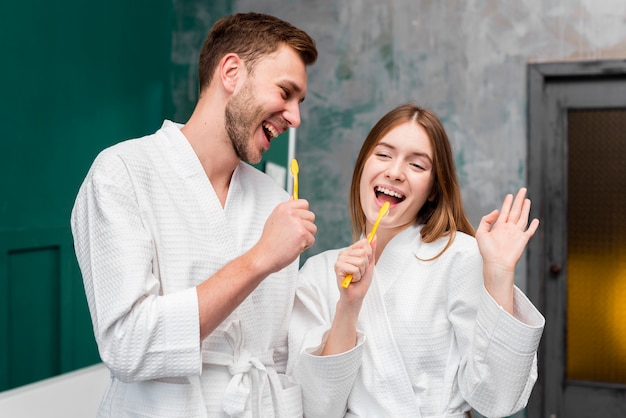 Paar im Bademantel mit Zahnbürsten herumalbern