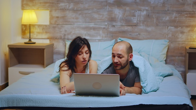 Paar im Pyjama im Bett liegend mit Laptop zum Einkaufen.