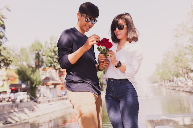 Paar in einem Park mit Rosen in den Händen und in den Sonnenbrillen