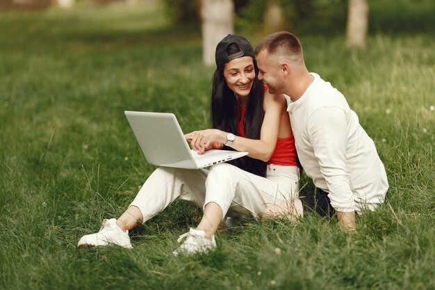 Paar in einer Frühlingsstadt. Dame mit einem Laptop. Leute sitzen auf einem Gras.