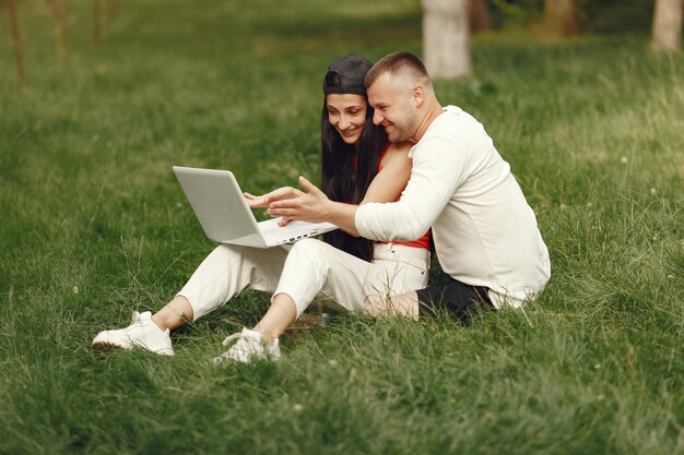 Paar in einer Frühlingsstadt. Dame mit einem Laptop. Leute sitzen auf einem Gras.