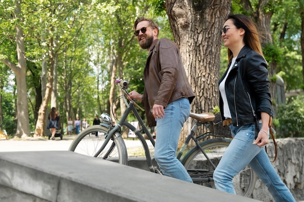 Paar in Kunstlederjacken, die mit Fahrrädern im Freien spazieren gehen