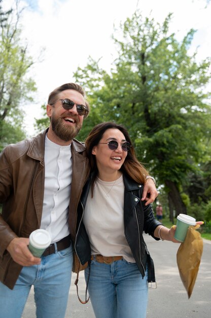 Paar in Kunstlederjacken mit Kaffee und Snacks beim Spaziergang im Freien