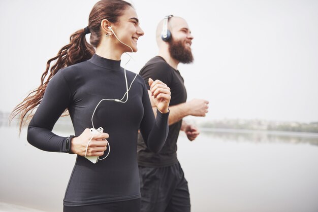 Paar Joggen und Laufen im Freien im Park in der Nähe des Wassers. Junger bärtiger Mann und Frau, die zusammen am Morgen trainieren