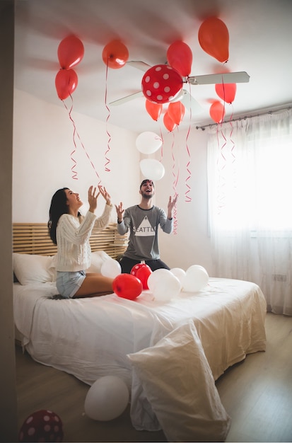 Paar lächelnd mit Händen erhabener Blick auf die Decke voller herzförmige Luftballons