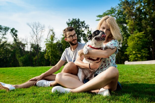 Paar lächelnd, sitzend auf Gras mit französischer Bulldogge im Park