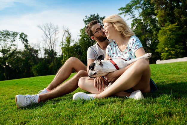 Paar lächelnd, sitzend auf Gras mit französischer Bulldogge im Park