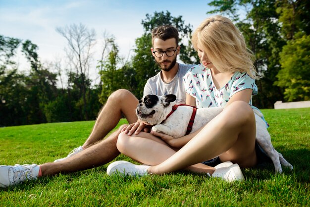 Paar lächelnd, sitzend auf Gras mit französischer Bulldogge im Park