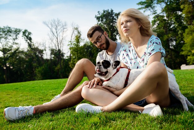 Paar lächelnd, sitzend auf Gras mit französischer Bulldogge im Park