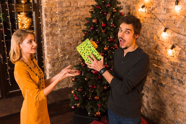 Paar mit Geschenkbox vor Weihnachtsbaum
