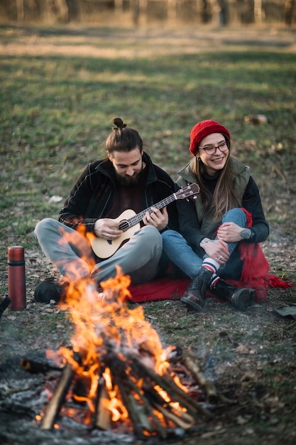 Paar mit Gitarre in der Nähe von Lagerfeuer