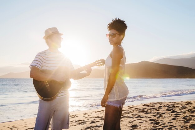 Paar mit Gitarre und Sonnenschein am Strand