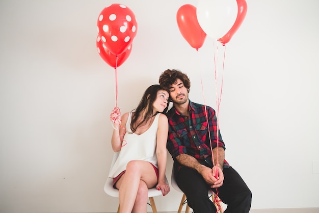 Kostenloses Foto paar mit luftballons in den händen auf weißen stühlen sitzen