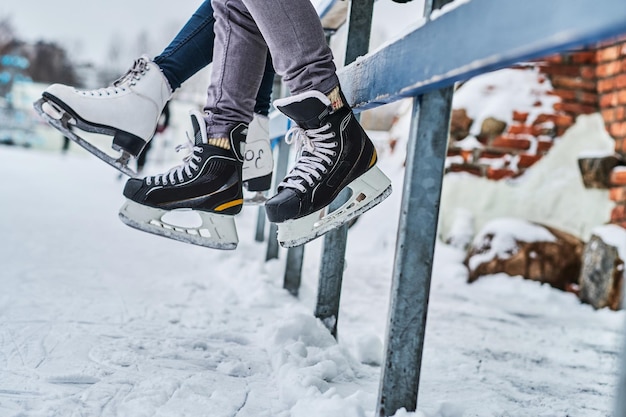 Paar mit Schlittschuhen sitzt auf einer Leitplanke. Dating in einer Eisbahn. Nahaufnahme der Schlittschuhe