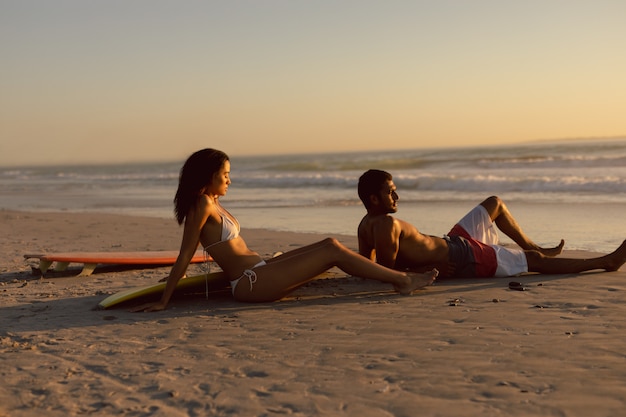 Paar mit Surfbrett am Strand in der Abenddämmerung entspannen