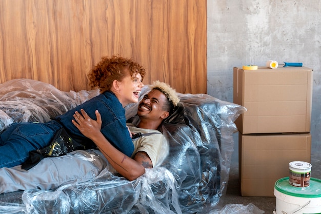 Paar ruht auf einem Sofa in ihrem neuen Zuhause neben Farbeimern