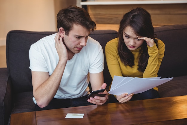 Paar sitzt auf dem Sofa und diskutiert mit Finanzdokumenten im Wohnzimmer