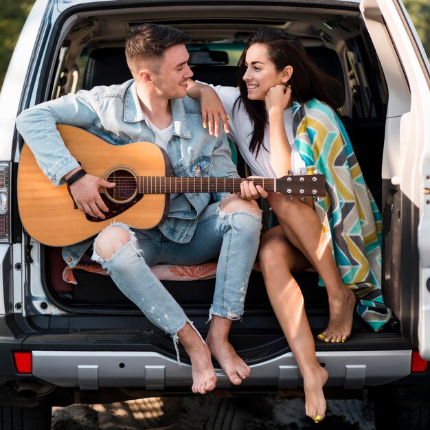 Paar sitzt im Kofferraum mit Gitarre